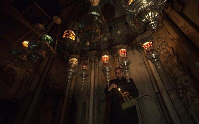 An Armenian Orthodox priest lights candles in the hanging oil lamps at the tomb of Jesus in the Holy Sepulchre church. (photo credit:AP/Dusan Vranic)