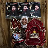 Missadeh Diab, 65, poses with presents made by her sons while they were in Israeli jails, at her home in the West Bank village of Kufr Rai. The posters in the background show her son Bilal and read in Arabic, "the strike will continue, Bilal Nabil Diab." (photo credit: AP/Bernat Armangue)