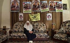 Dalal, mother of Mohammed al-Taj, sits underneath posters showing her son at their family house in the West Bank village of Tubas. (photo credit: AP/Bernat Armangue)