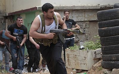 A Sunni gunman runs with his weapon during clashes in the northern port city of Tripoli, Lebanon, this month (photo credit: Hussein Malla/AP)