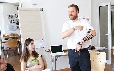 Rabbi Josh Ahrens demonstrates how to put on tefillin during a conversion course at the Sofia JCC in Bulgaria. (Dianna Cahn)