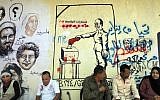 Egyptians sit in front of graffiti showing faces of people killed in the 2011 revolution, right, and the head of the Supreme Council of the Armed Forces, Field Marshal Hussein Tantawi, casting his vote, center, in Tahrir Square in Cairo, Egypt, Friday (photo credit: AP/Amr Nabil)