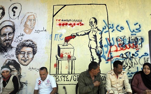 Egyptians sit in front of graffiti showing faces of people killed in the 2011 revolution, right, and the head of the Supreme Council of the Armed Forces, Field Marshal Hussein Tantawi, casting his vote, center, in Tahrir Square in Cairo, Egypt, Friday (photo credit: AP/Amr Nabil) Egyptians sit in front of graffiti showing faces of people killed in the 2011 revolution, right, and the head of the Supreme Council of the Armed Forces, Field Marshal Hussein Tantawi, casting his vote, center, in Tahrir Square in Cairo, Egypt, Friday (photo credit: AP/Amr Nabil)