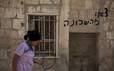 A woman walks past the Jerusalem apartment that had been set on fire on Monday. Spray-painted message reads 'get out of the neighborhood' (photo credit: Yonatan Sindel/Flash90)