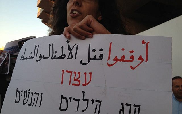 A sign in Arabic and Hebrew reads 'stop the killing of children and women' (photo credit: Elhanan Miller/Times of Israel)