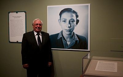 Holocaust survivor Michael Pupa standing next to his childhood photo in the "Attachments" exhibit at the National Archives in Washington, DC. (photo credit: Earl McDonald for the National Archives/JTA)