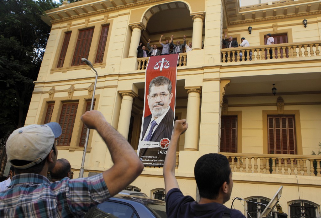 Egyptian supporters of the Muslim Brotherhood's candidate, Mohammed Morsi, celebrate next to a giant poster of him at his campaign headquarters in Cairo, Egypt. (photo credit: AP/Amr Nabil)