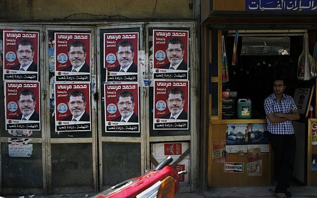 A worker stands in front of his shop next to posters with pictures of presidential candidate Mohammed Morsi in Cairo, Egypt, Wednesday (photo credit: Nasser Nasser/AP)