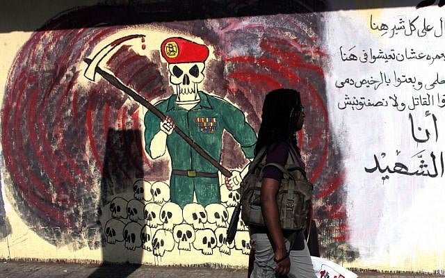 A woman passes a wall with graffiti depicting the ruling military council and Arabic that reads, "you sold my blood cheap, you supported the killer but not me, I am the martyr," in Cairo on Thursday. (photo credit: AP/Nasser Nasser)