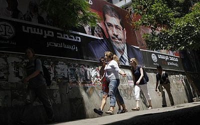Tourists walk past a campaign poster supporting Egyptian presidential candidate Mohammed Morsi in Cairo (photo credit: AP Photo/Amr Nabil)
