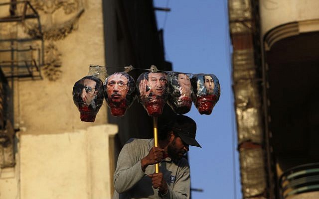 An Egyptian protester carries symbolic heads depicting ousted President Hosni Mubarak, center, and from left, his son Alaa, his interior minister Habib al-Adly, wife Suzanne and son Gamal during a rally protesting the outcome of the Mubarak trial at Tahrir Square, Cairo, Egypt, Tuesday (photo credit: AP/Nasser Nasser)