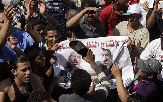 Egyptian protesters use their shoes to strike a poster showing ousted president Hosni Mubarak and presidential candidate Ahmed Shafiq during a protest at Tahrir Square, Cairo, Egypt, on Friday (photo credit: AP/Amr Nabil)