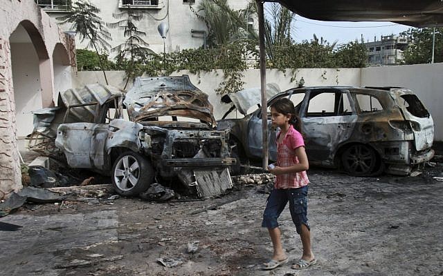 A Gazan girl walks passed a car destroyed in an IAF airstrike Wednesday (photo credit: AP/Adel Hana)