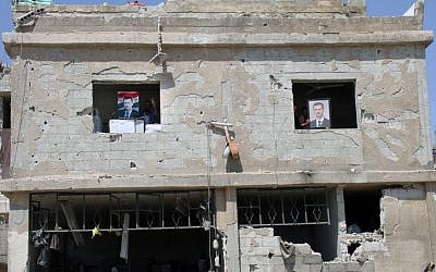 Syrian security forces officers hold portraits of Syrian President Bashar Assad from the windows of their building, which was destroyed after a car bomb exploded near the shrine of Sayyida Zeinab, in a suburb of Damascus, Syria. (photo credit: AP)