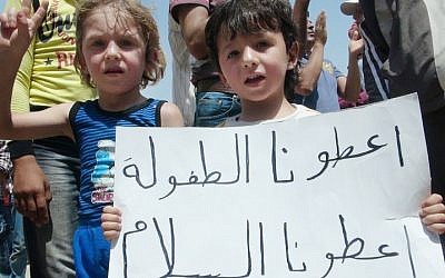 Syrian children hold a poster that reads, "Give us a childhood give us peace, and that's all," during a demonstration in Idlib. (photo credit: Local Coordination Committees in Syria/AP)