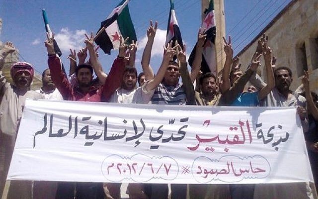 Anti-Syrian regime protesters chant slogans and hold a banner in Arabic that reads, "Al-Qubair massacre challenges the world's humanity," during a protest against the massacre of Mazraat al-Qubair on Thursday. (Photo credit: AP/Edlib News Network ENN)