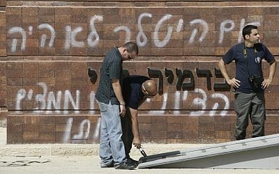 Men clean up graffiti spray painted at Yad Vashem (photo credit: Uri Lenz/Flash90)