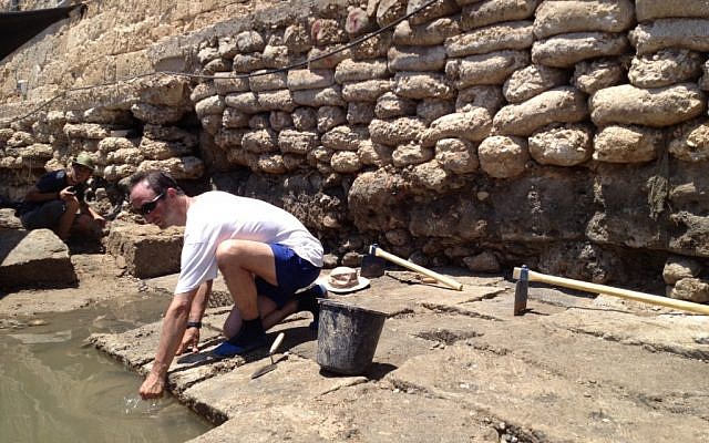 An Israel Antiquities Authority worker kneels on the newly uncovered 2,300-year-old pier (photo credit: Matti Friedman/Times of Israel)