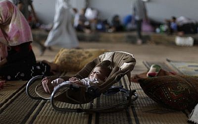 A Syrian child lies in a safety seat while his family takes refuge at the Bab Al-Salameh border crossing, in hopes of entering one of the refugee camps in Turkey. (file photo credit: AP/Muhammed Muheisen)