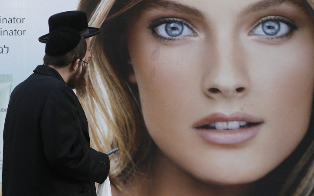 An Ultra Orthodox Jewish man walks past a poster showing a woman, in Jerusalem.Dec. 13, 2011. A new range of products aim to prevent men from seeing immodest women by reducing their vision. (photo credit: Uri Lenz / Flash90)