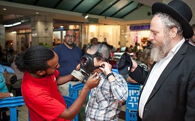 A postal worker helps a child try on a gas mask in Jerusalem. (photo credit: Noam Moskowitz/Flash90)