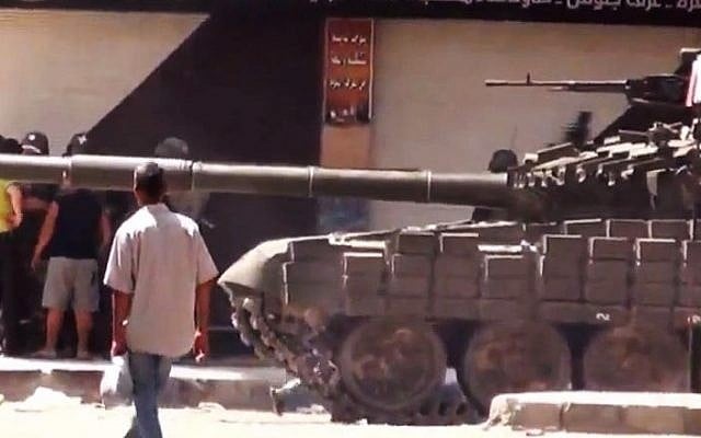 This image released by Shaam News Network purports to show a man walking past Syrian a military tank in Damascus, Syria. The Assad regime has allegedly been using heavy weapons against civilians. (photo credit: AP/Shaam News Network/AP video)