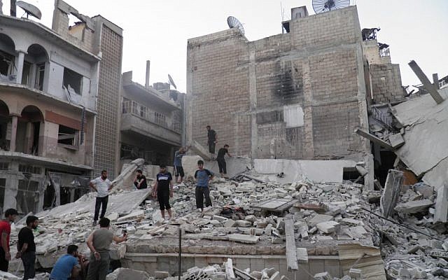 This image purports to show Syrians standing in the rubble of a destroyed building from Syrian forces shelling in Khaldiyeh neighborhood, Homs province, central Syria. (photo credit: AP/Shaam News Network, SNN)