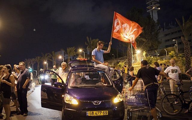 A demonstrator waves a flag at one of two protests Saturday night in Tel Aviv (photo credit: Tali Mayer /Flash90)