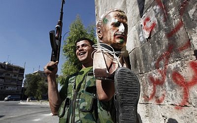 A Free Syrian Army soldier holds up a bust of Hafez Assad tied to a shoe, a symbol of humiliation in Aleppo, September 24 (photo credit: AP/Hussein Malla)