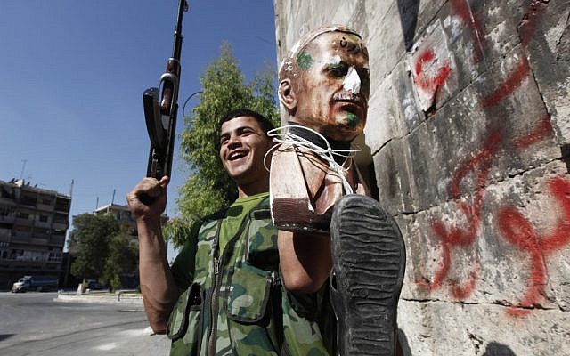 A Free Syrian Army soldier holds up a bust of Hafez Assad tied to a shoe, a symbol of humiliation in Aleppo, September 24 (photo credit: AP/Hussein Malla)
