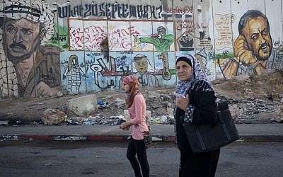 Palestinian women pass by a mural depicting late Palestinian Authority president Yasser Arafat and jailed Tanzim leader Marwan Barghouti at the Qalandiya checkpoint. (Yonatan Sindel/Flash90)