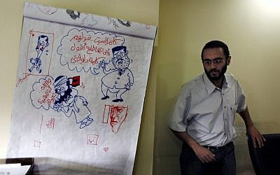 Egyptian cartoonist Abdul-Rahman Najmuddin walks past cartoon sketches, one depicting Egyptian president Mohammed Morsi with a caption in Arabic "someone calls home and tell them that I am delivering a speech," at Al Watan daily newspaper headquarters in Cairo on Wednesday. (photo credit: AP/Nasser Nasser)