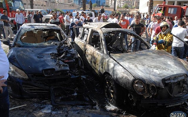 A firefighter extinguishes a burned car close to where an explosion went off between the buildings of the Ministry of Information and the Ministry of Justice in Damascus, Syria. (photo credit: AP Photo/SANA)