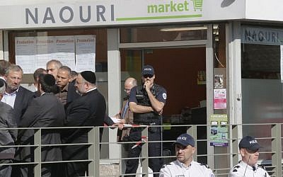 Police and members of the Jewish community stand in front of a kosher supermarket in Sarcelles, north of Paris, where a bomb exploded last month (photo credit: AP/Michel Euler)