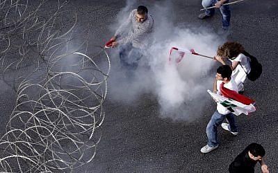 Lebanese protesters are enveloped in tear gas as they pull a barbed-wire barrier during clashes after the funeral of Brig. Gen. Wissam al-Hassan who was assassinated on Friday by a car bomb in Beirut, Lebanon, Sunday Oct. 21 (photo credit: AP/Hussein Malla)
