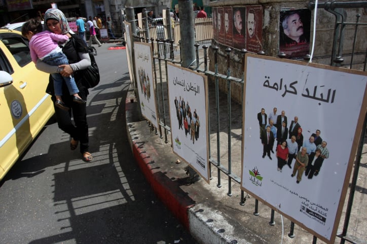 A Palestinian woman carries her baby past campaign posters in Ramallah on the first day of campaigning for local elections on October 6, 2012. (Issam Rimawi/Flash90) A Palestinian woman carries her baby past campaign posters in Ramallah on the first day of campaigning for local elections on October 6. (photo credit: Issam Rimawi/Flash90)