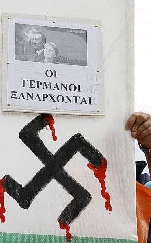 A demonstrator holds a banner with an image of Nazi leader Adolf Hitler and present German Chancellor Angela Merkel with a swastika and a slogan that reads " the Germans are coming back" prior to an protest in Athens. (photo credit: AP/Lefteris Pitarakis)