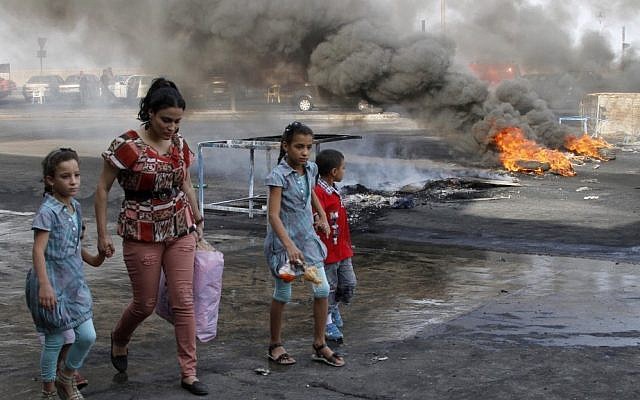A family walks past flaming tires used as a roadblock to protest the death of Brig. Gen. Wissam al-Hassan, head of the intelligence division of Lebanon's domestic security forces in a car bomb attack targeting his convoy, in the southern port city of Sidon, Lebanon on Saturday. (photo credit: AP Photo/ Mohammed Zaatari)