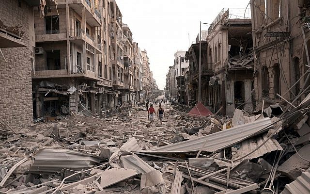 Syrian men walk at a street between destroyed buildings where triple bombs rocked at the Saadallah al-Jabri square in Aleppo on Wednesday. (photo credit: AP/SANA) Syrian men walk at a street between destroyed buildings where triple bombs rocked at the Saadallah al-Jabri square in Aleppo on Wednesday. (photo credit: AP/SANA)