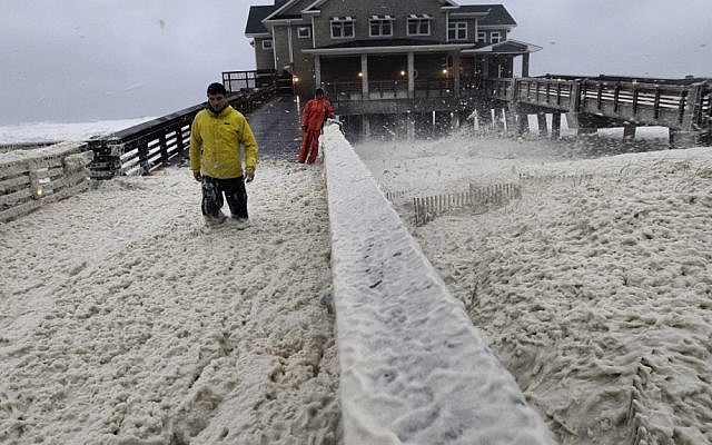 A news crew wades through sea foam in Nags Head, North Carolina, on Sunday, as wind and rain from Hurricane Sandy move into the area. (photo credit: AP/Gerry Broome)