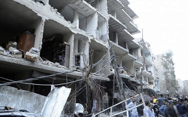 In this image released by the Syrian official news agency, a crowd gathers beneath the shattered facade of a building damaged by a car bomb in Damasus, Syria Friday. (photo credit: AP)