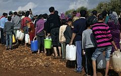Syrian refugees line up to fill plastic containers with water at a displaced persons camp near the Turkish border, November 2012 (photo credit: AP/Khalil Hamra/File)