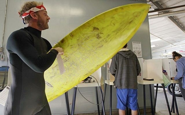After voting, Mike Weigart, 30, carries his ballot and his surfboard to the ballot box at the polling place at the Venice Beach lifeguard headquarters in Los Angeles Tuesday, Nov. 6, 2012. Weigart said "It's awesome the polling place is where I surf." (AP Photo/Reed Saxon)