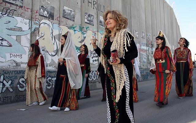 Palestinian Christian women wearing traditional clothes walk past the Israeli separation barrier or wall in the West Bank town of Bethlehem, as Christmas approaches, on December 23, 2010. (photo credit: Najeh Hashlamoun/Flash90)