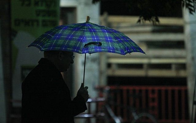 A Jerusalem man takes cover from the rain on Friday night. (photo credit: Oren Nahshon / FLASH90)