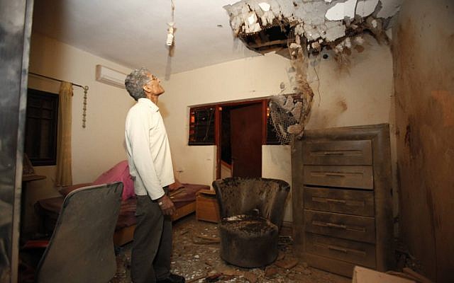 An Israeli man examines the damage to his daughter's bedroom after a Kassam rocket fired by Palestinian terrorists from Gaza hit his house in the southern town of Sderot on November 11 (photo credit: Edi Israel/Flash90)