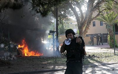 A police officer shoos away onlooker coming to view a vehicle that caught fire after suffering a hit by a rocket fired from Gaza, in Ashkelon, on Sunday, November 18 (photo credit: Yossi Zamir/Flash90) A police officer shoos away onlooker coming to view a vehicle that caught fire after suffering a hit by a rocket fired from Gaza, in Ashkelon, on Sunday, November 18 (photo credit: Yossi Zamir/Flash90)