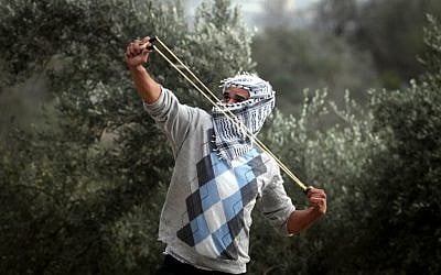 A Palestinian student from the Birzeit University covers his face as he uses a slingshot to throw stones at Israeli troops during clashes with Israeli soldiers at the Atara checkpoint close to their university as they protest against Israel's military action on the Gaza Strip. November 19, 2012 (photo credit: Issam Rimawi/Flash90)