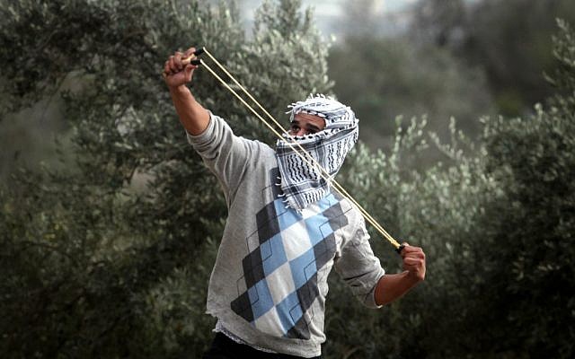 A Palestinian student from the Birzeit University covers his face as he uses a slingshot to throw stones at Israeli troops during clashes with Israeli soldiers at the Atara checkpoint close to their university as they protest against Israel's military action on the Gaza Strip. November 19, 2012 (photo credit: Issam Rimawi/Flash90)