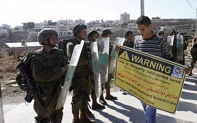 A Palestinian protester holds a placard in front of Israeli soldiers during a demonstration in the West Bank village of al-Masara near Bethlehem, marking the recognition of a sovereign Palestinian state by the United Nations. Friday Nov. 30 (photo credit: AP/Nasser Shiyoukhi)